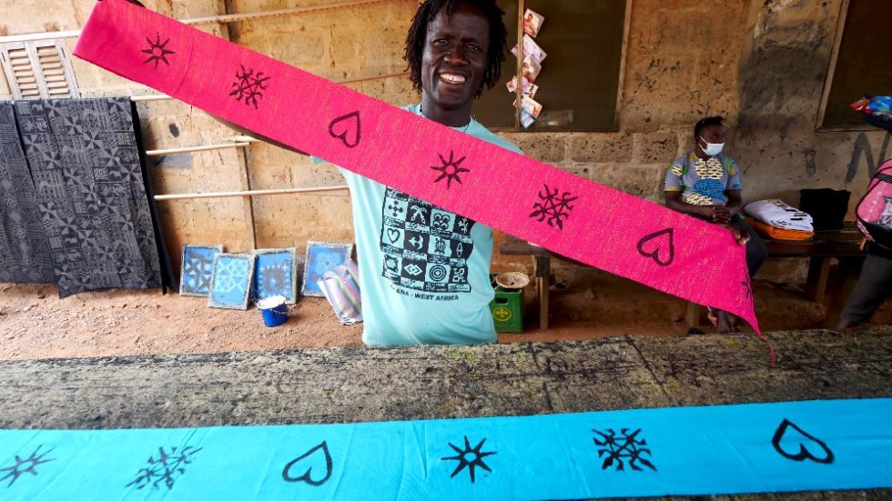 Man holding stamped pink and blue cloths with three symbols in African market