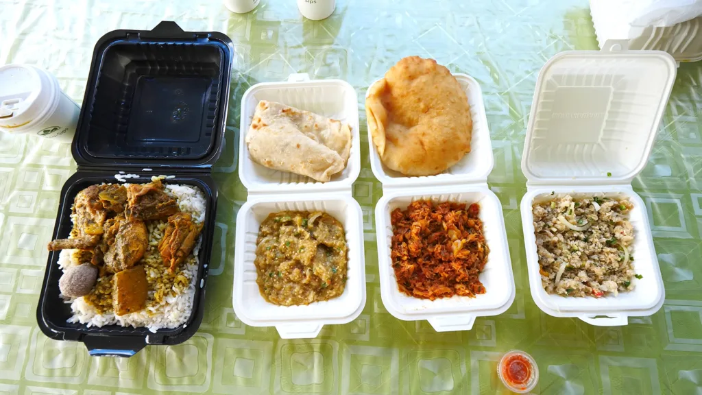 A spread of Caribbean food dishes, including pachownie, roti, saltfish, bake, baigan choka, and chicken curry with dal and rice | Davidsbeenhere